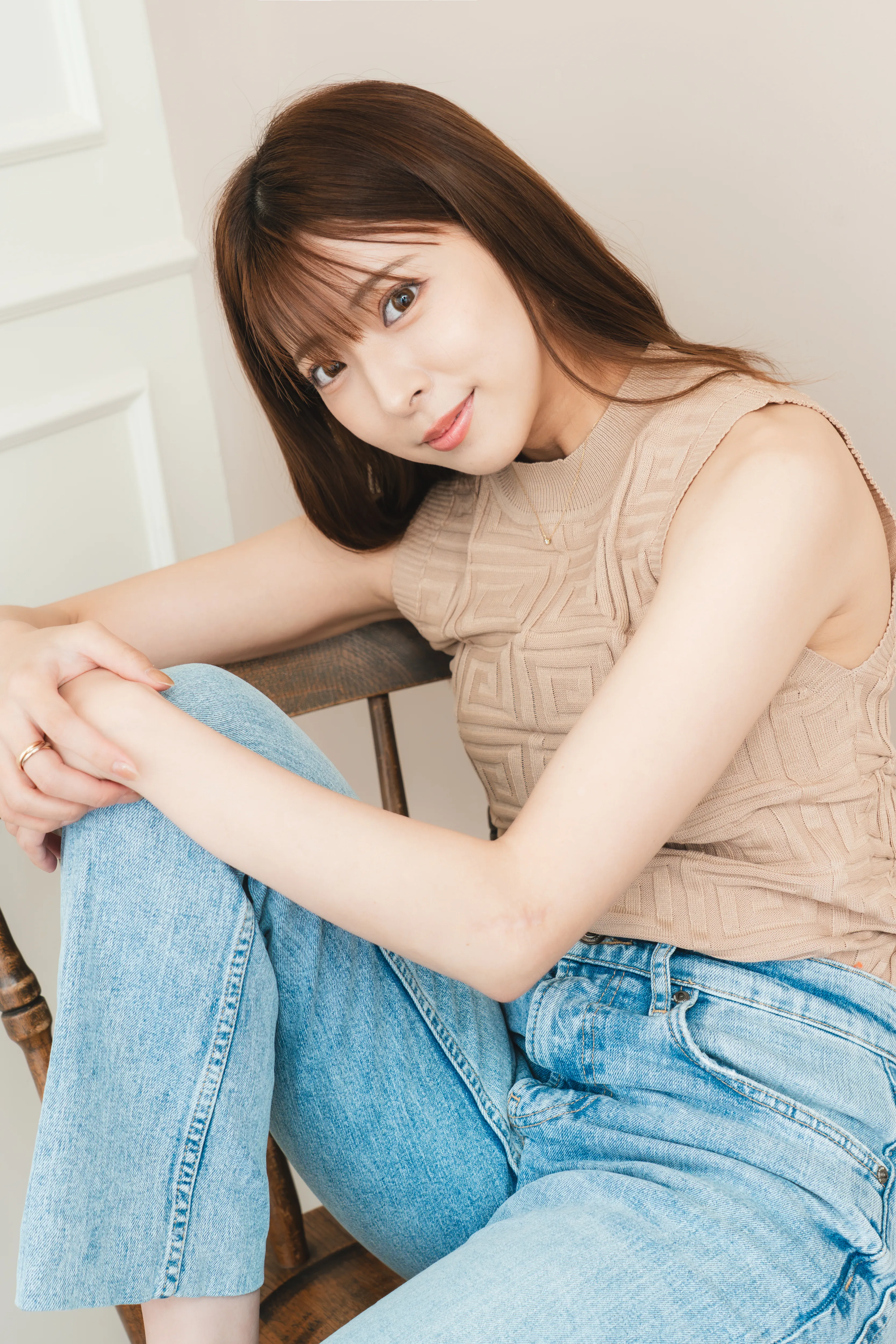 ベージュのトップスとデニム姿で椅子に座る榎本千紘様のポートレート