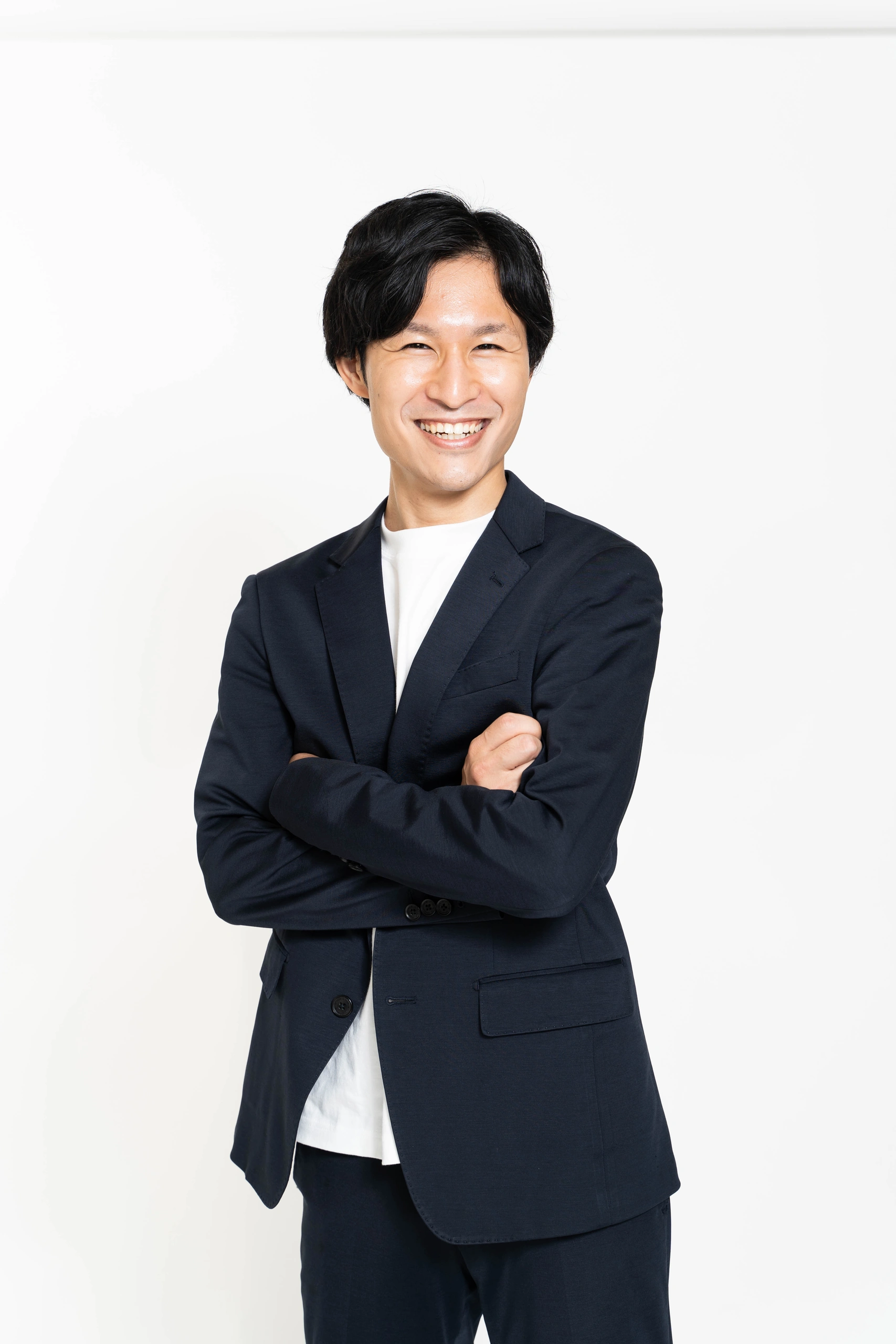 白い背景で紺色のスーツを着て腕を組む人物